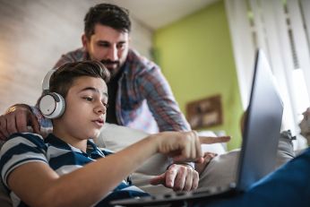 A boy is looking at his computer and gets help from his father. 