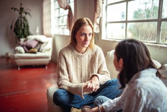 Zwei Frauen sitzen auf einer Couch und sprechen miteinander.