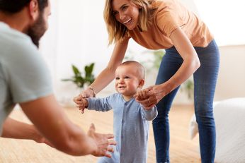 Eltern mit einem Baby. Das Baby versucht das erste Mal zu gehen.