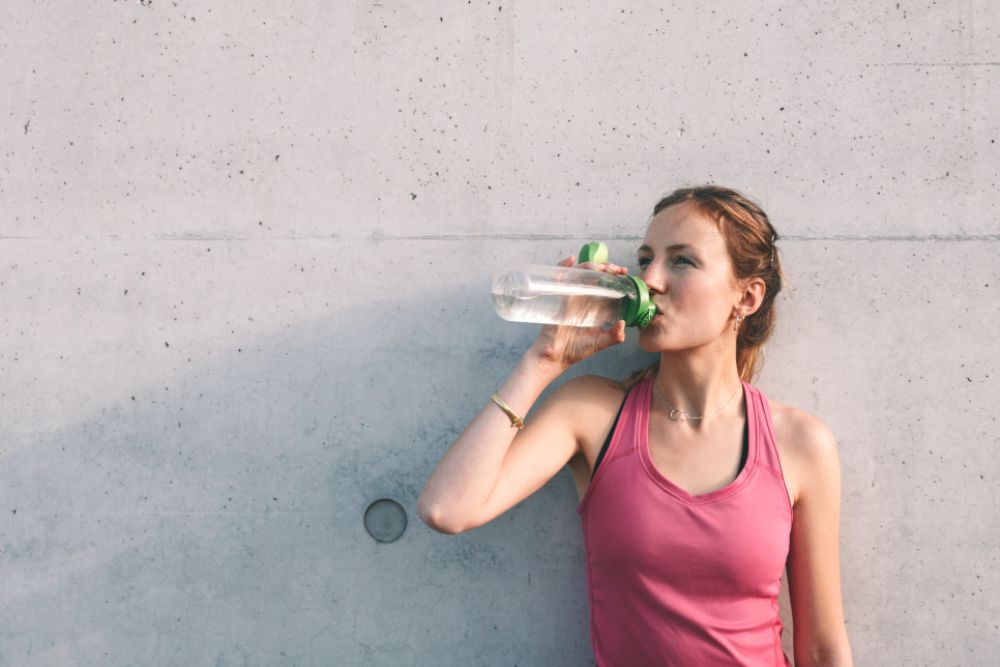 Frau trinkt aus einer Flasche. Sie trägt Sportkleidung.