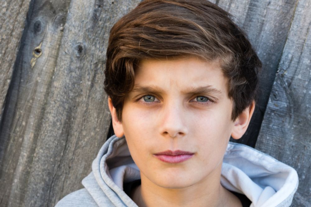 Junge mit braunen Haaren. Er blickt ernst in die Kamera.