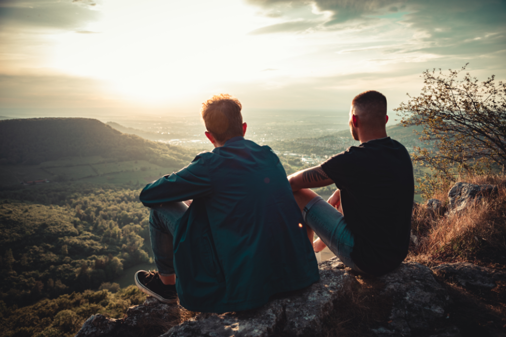 Two Men are sitting side by side. They are watching the sunset. 