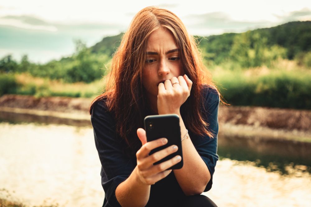 A young woman looks scared at her mobile phone.