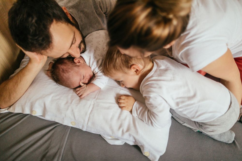 Vater und Mutter liegen mit ihren zwei kleinen Kindern im Bett.