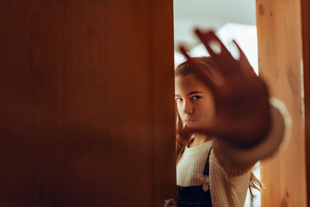 Mädchen steht hinter einer Türe. Sie hält selbstbewusst ihre Hand vor ihr Gesicht und symbolisiert damit "Stop".