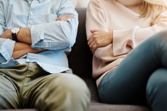 Eine Frau und ein Mann sitzen auf einem Sofa. Beide verschränken ihre Arme. 