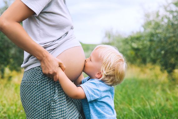 Ein Kind gibt einer schwangeren Frau einen Kuss auf den Bauch. 