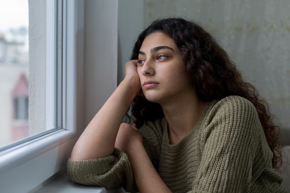 Frau schaut schwermütig aus dem Fenster.