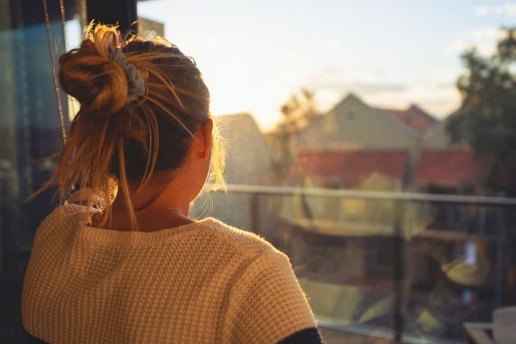 Frau schaut aus Fenster in die Ferne