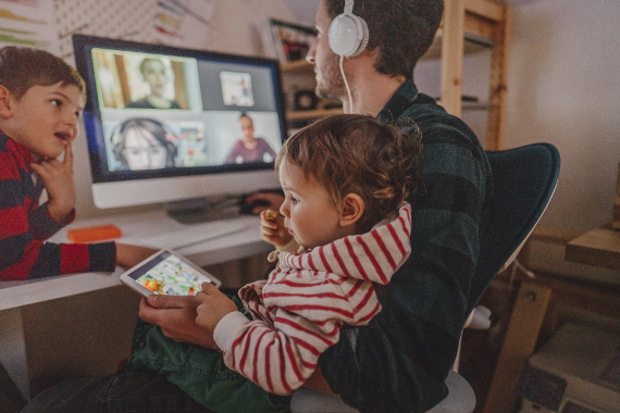 A man is taking an online meeting. His two children are by his side. 