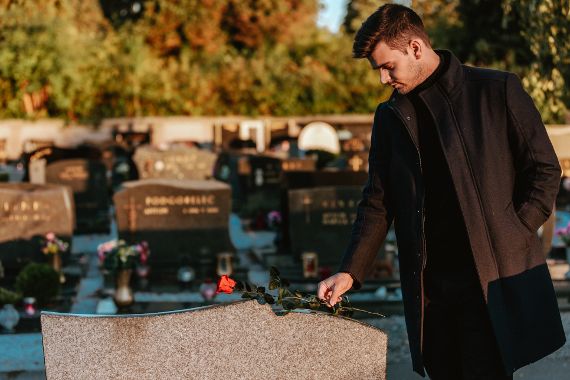 Man putting a rose on a gravestone.